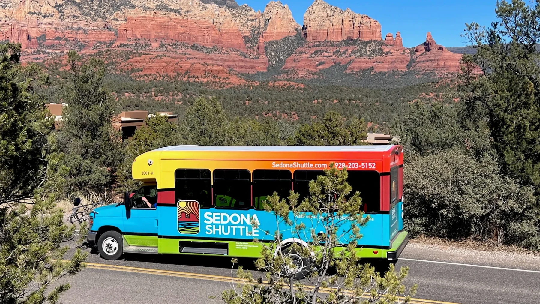 A colorful Sedona Shuttle bus beside desert vegetation