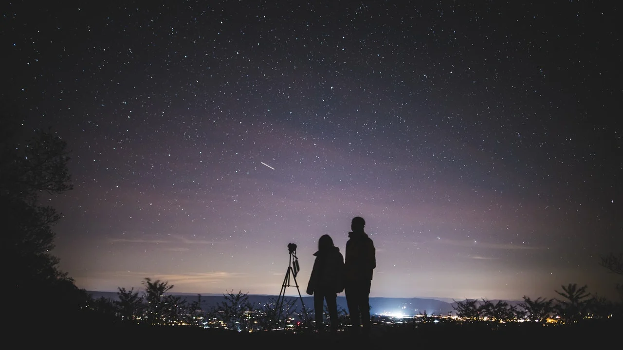 Two people beside a telescope beneath a star-filled sky