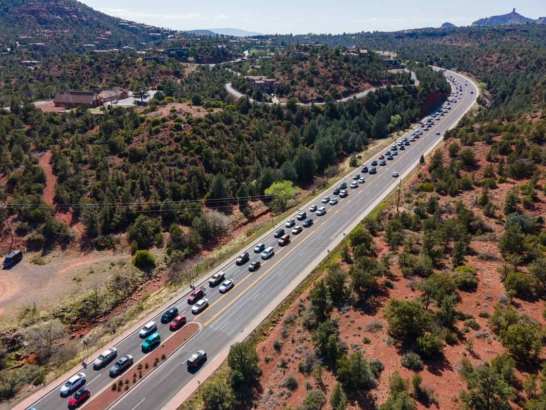 A line of traffic on a road through wooded red-rock country