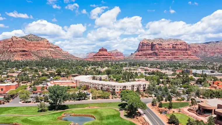 Aerial view of buildings and green grounds below red-rock formations