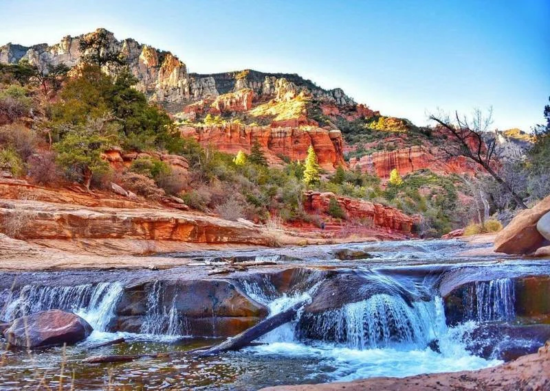 Water cascading over rock ledges below a red canyon wall