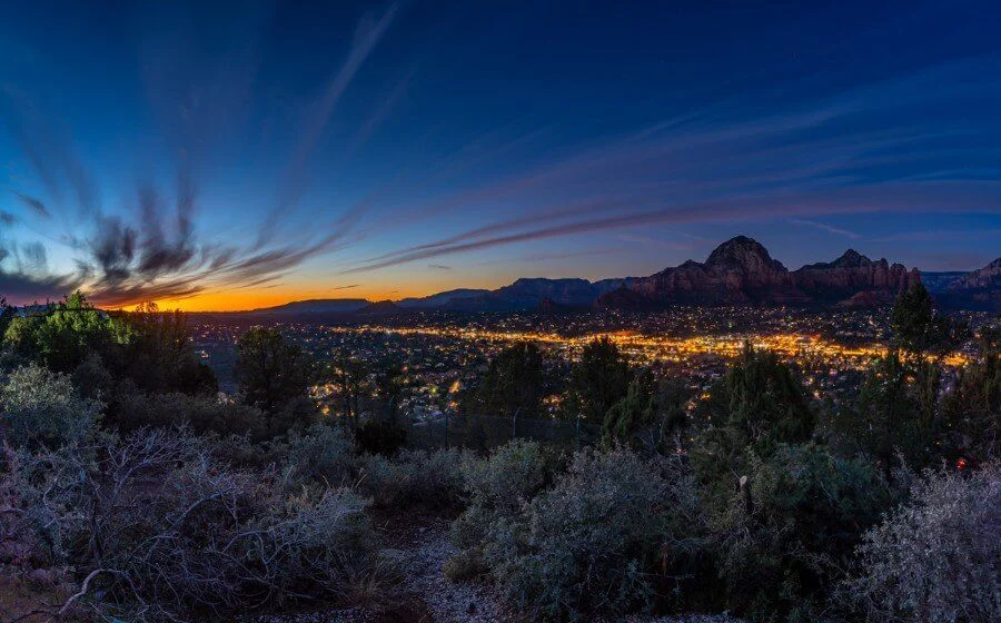 City lights beneath a deep blue evening sky and distant red rocks
