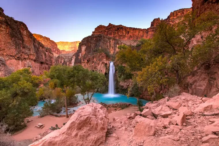 A waterfall dropping into turquoise water beneath canyon walls